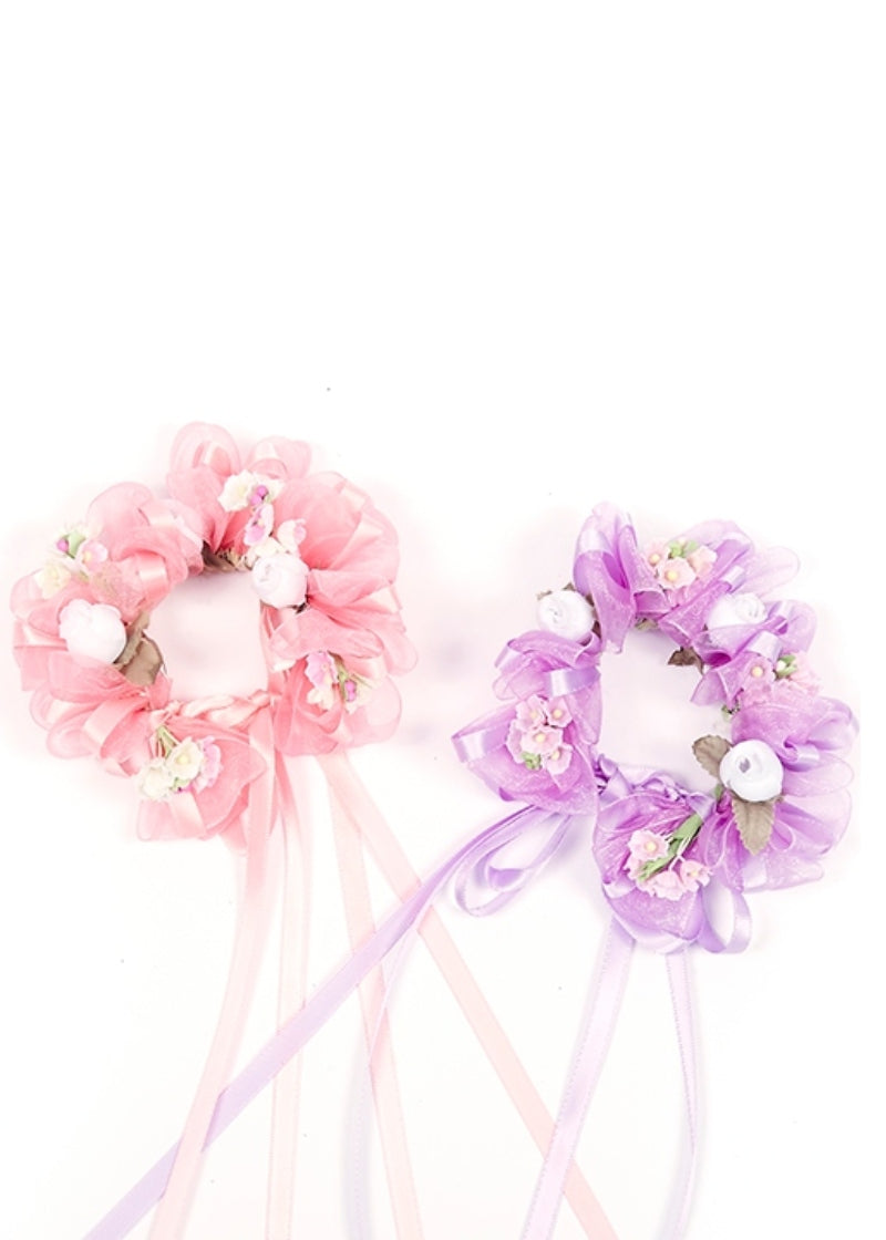 Two bunrings made with satin and sheer ribbon, including ribbon trains. One is pink, one is lilac, and they both have pink and white flowers on the rings.