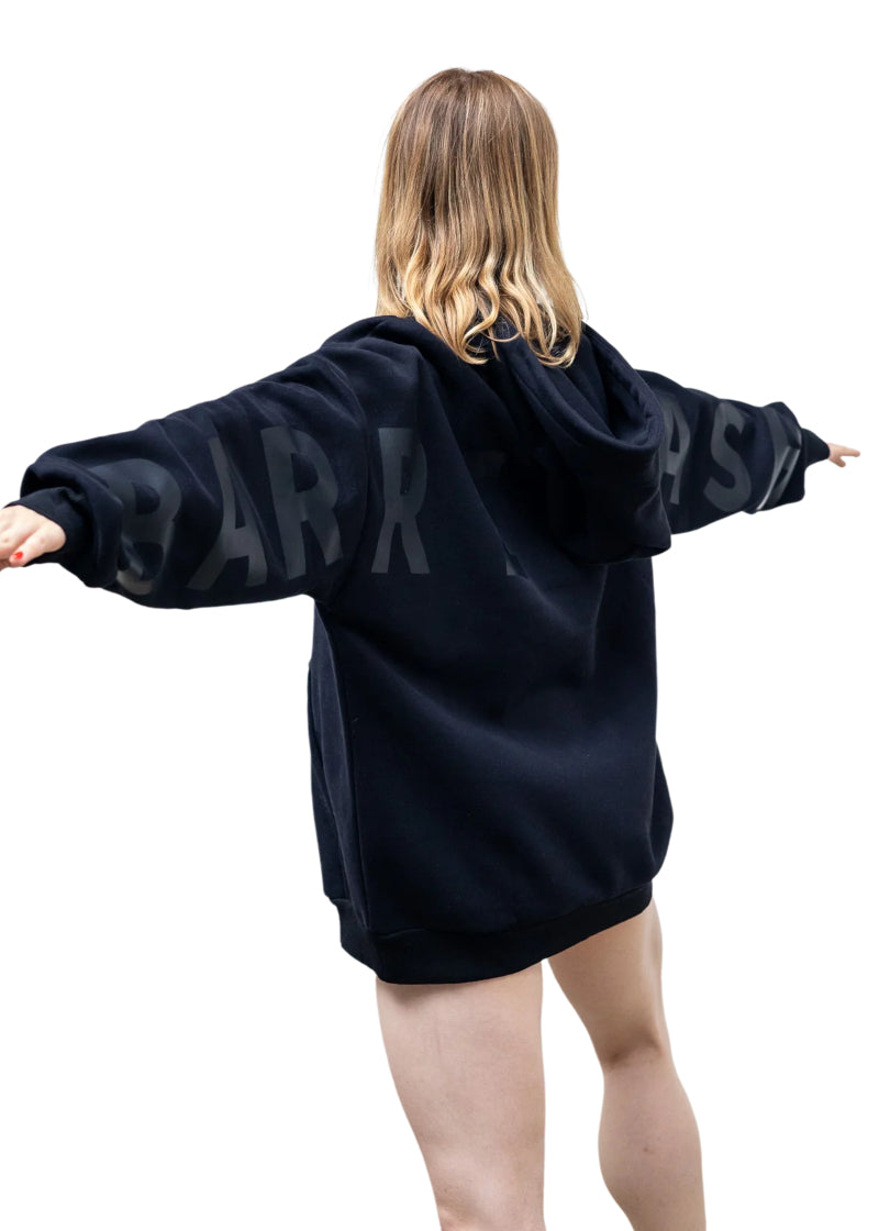 Barre Trash OH Oversized Hoodie in Black on Black, modeled by a ballet dancer with BARRE TRASH in black lettering across the sleeves & back