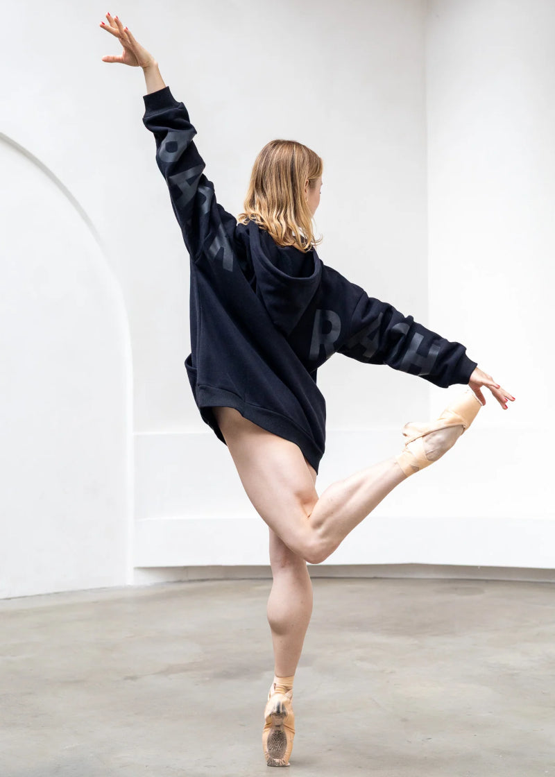 Barre Trash OH Oversized Hoodie in Black with the BARRE TRASH logo in Black, modeled by a ballet dancer