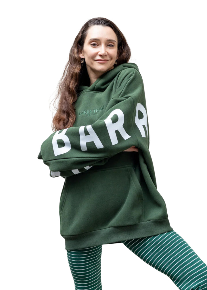 Barre Trash OH Women's Oversized Hoodie in Emerald Green with white Barre Trash logo across the sleeves and back, modeled by a ballet dancer
