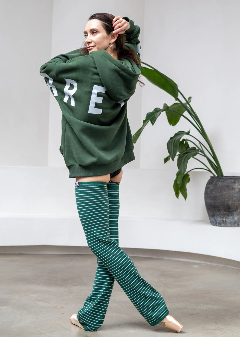Barre Trash OH Women's Oversized Hoodie in Emerald Green with white Barre Trash logo across the sleeves and back, modeled by a ballet dancer in a studio with a monstera in the background
