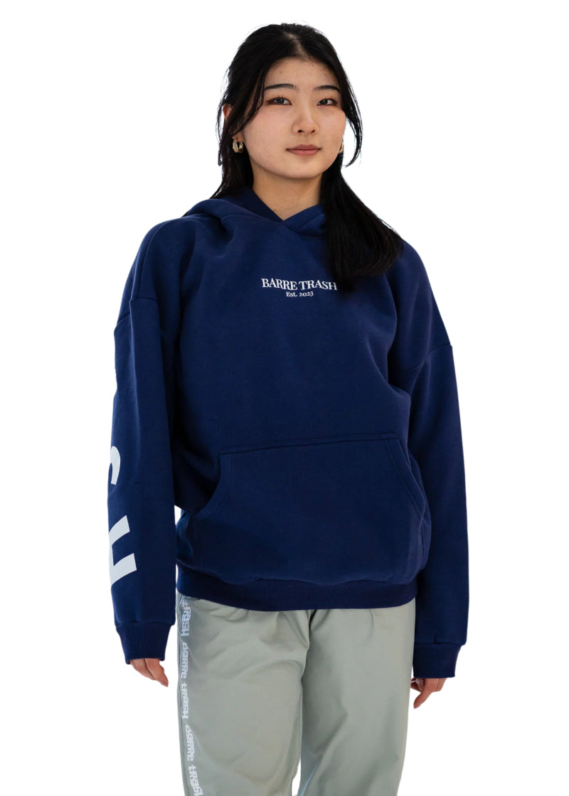Barre Trash OH Women's Oversized Hoodie in Mariner Navy Blue with the Barre Trash logo in white lettering across the sleeves & back, modeled by a ballet dancer