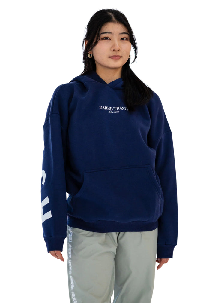 Barre Trash OH Women's Oversized Hoodie in Mariner Navy Blue with the Barre Trash logo in white lettering across the sleeves & back, modeled by a ballet dancer