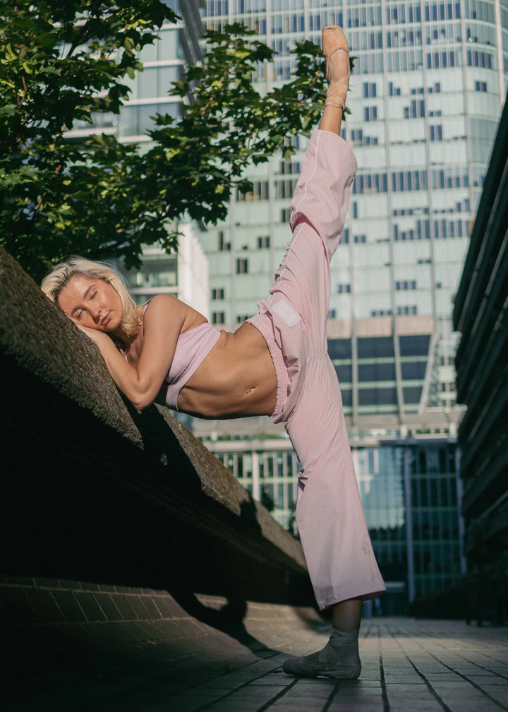 Barre Trash TSP Tracksuit Pants in Ballerina Pink, modeled by a ballet dancer en pointe with a cityscape in the background