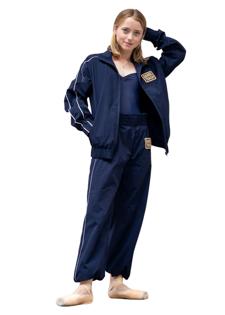 Barre Trash TSP Tracksuit Pants in Navy Blue with white side stripes and adjustable drawstring leg openings, modeled by a ballet dancer