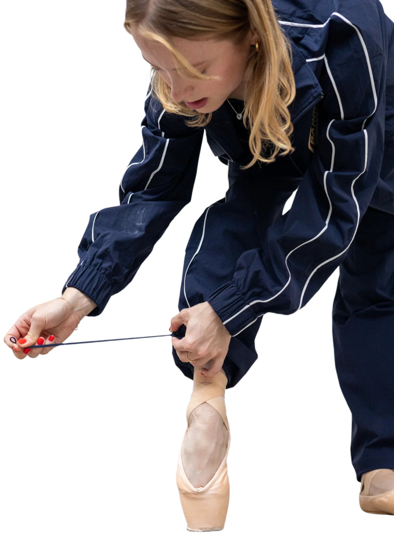 Barre Trash TSP Tracksuit Pants in Navy Blue with white side stripes and adjustable drawstring leg openings, modeled by a ballet dancer