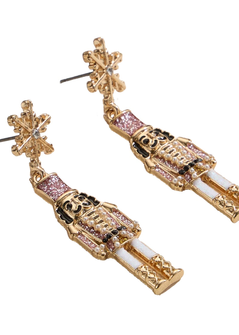 gold plated holiday nutcracker shaped earrings with pink and white enamel hanging from a snowflake-shaped post
