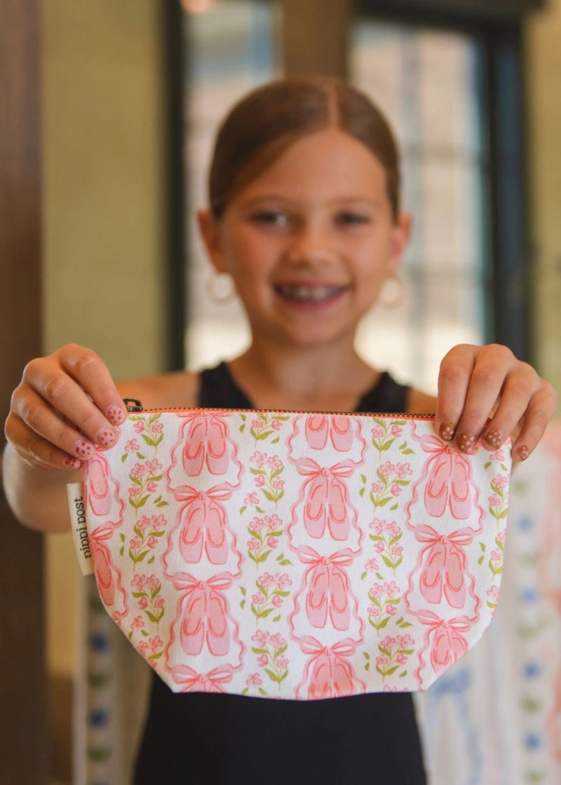 Dancer holding ballet slipper and pink and green floral patterned canvas accessory bag.