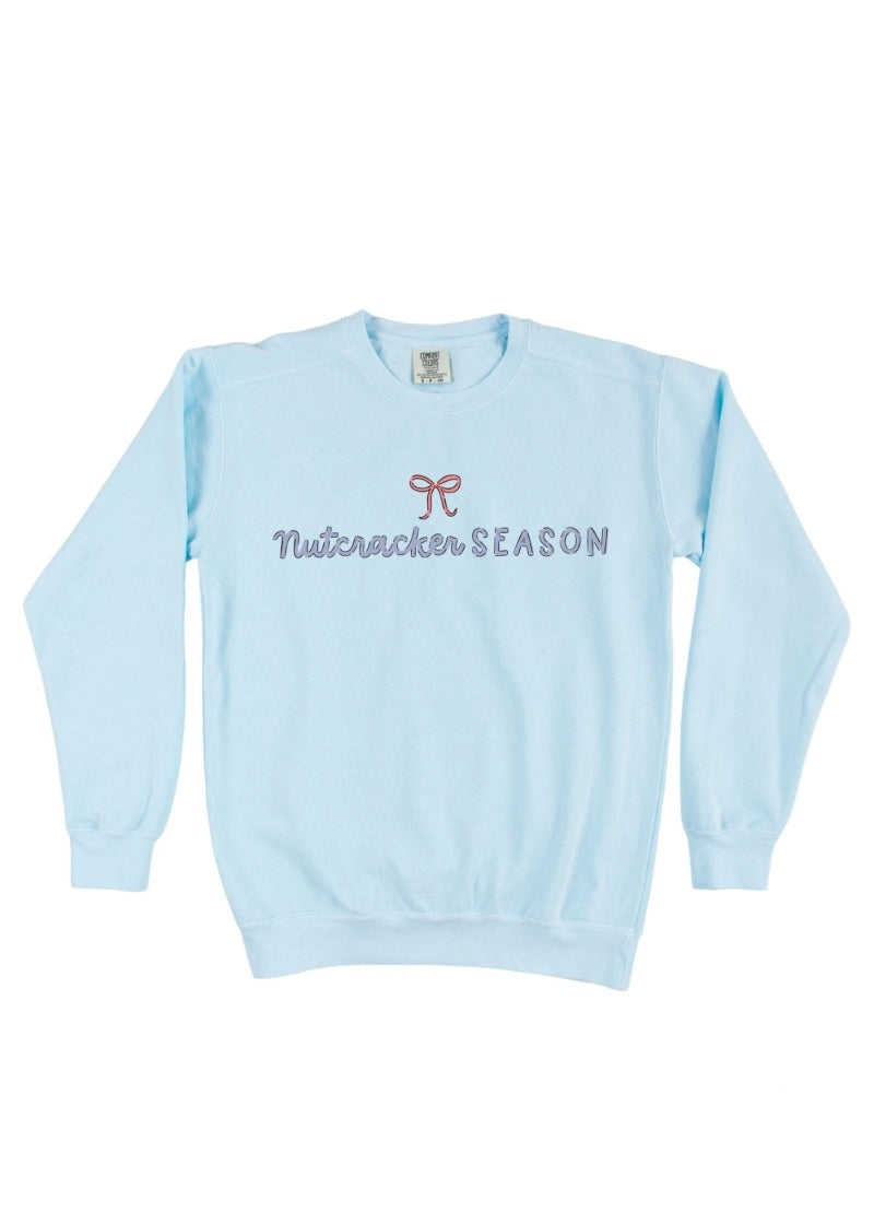 Light blue crew neck sweatshirt with "Nutcracker SEASON" text and pink bow graphic.