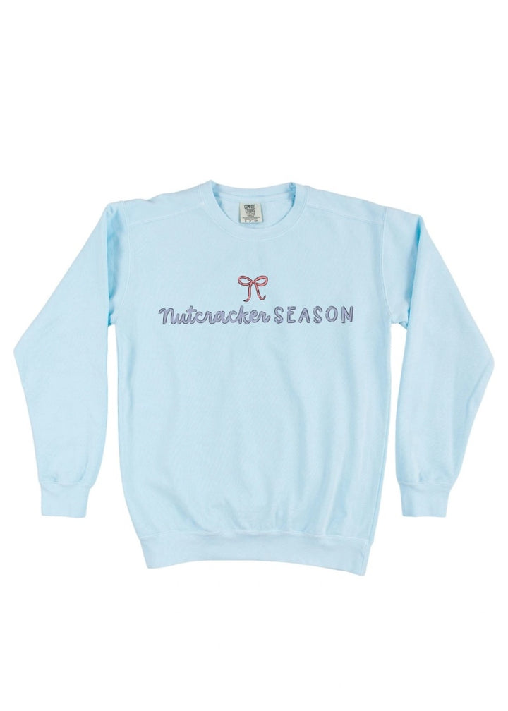 Light blue crew neck sweatshirt with "Nutcracker SEASON" text and pink bow graphic.